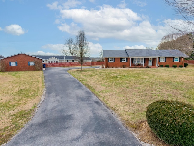 ranch-style home with aphalt driveway, a front yard, covered porch, and brick siding