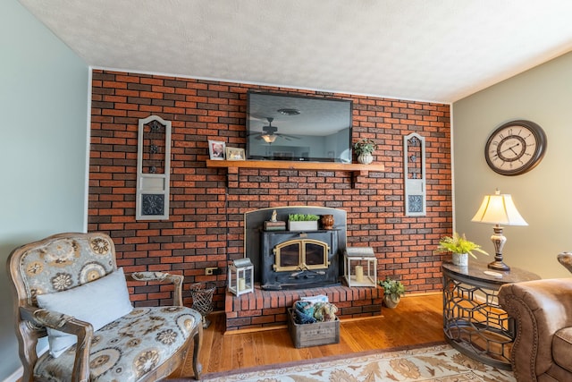 living area featuring a wood stove, brick wall, a textured ceiling, and wood finished floors