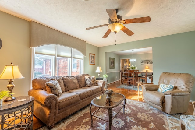 living room featuring a textured ceiling, ceiling fan, wood finished floors, and baseboards