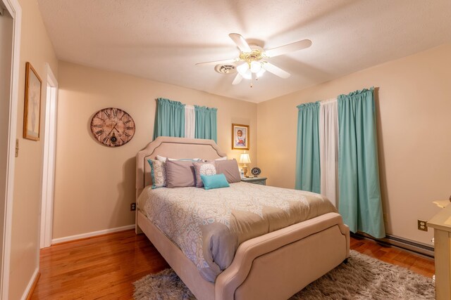 bedroom with ceiling fan, a baseboard heating unit, wood finished floors, and baseboards