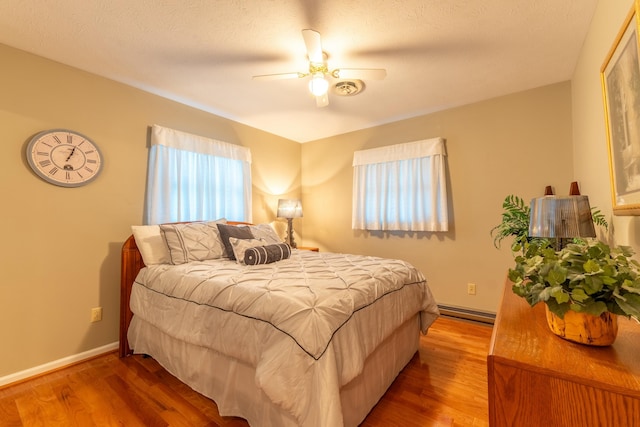 bedroom featuring a ceiling fan, baseboards, baseboard heating, and wood finished floors