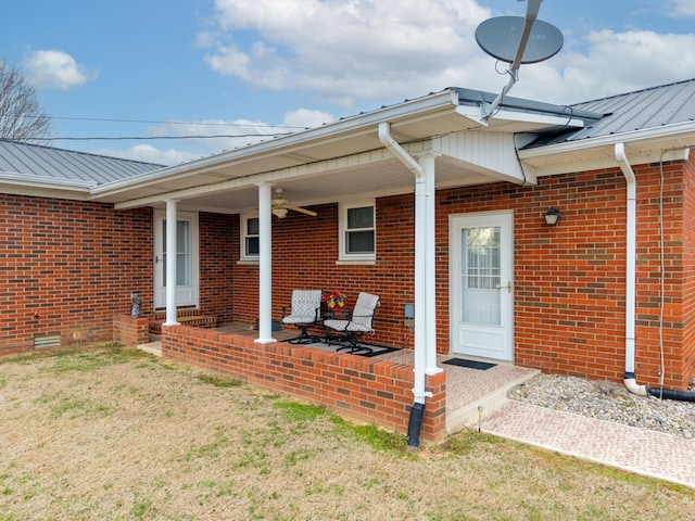 view of exterior entry featuring a standing seam roof, brick siding, a lawn, and metal roof