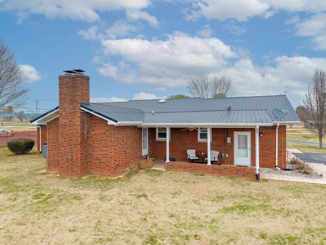 back of property featuring a yard, a chimney, metal roof, and brick siding