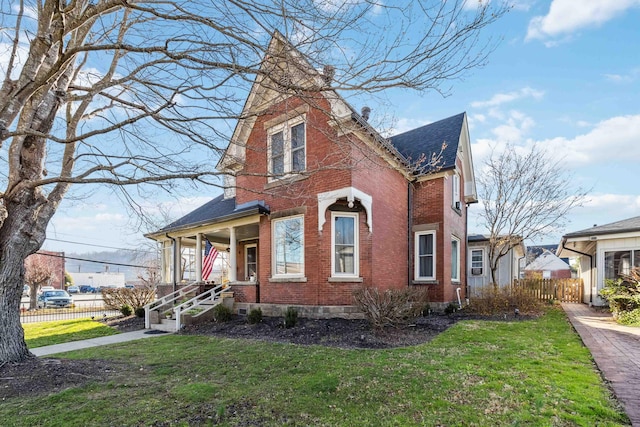 view of front of property with a front lawn, fence, brick siding, and a shingled roof