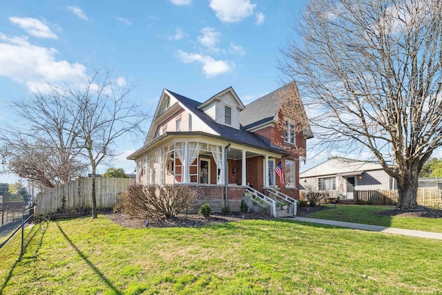 view of front of property featuring brick siding, covered porch, a front lawn, and fence