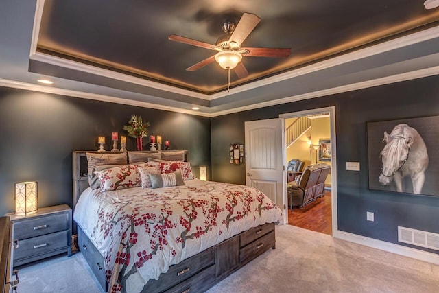 carpeted bedroom featuring a tray ceiling, crown molding, visible vents, a ceiling fan, and baseboards