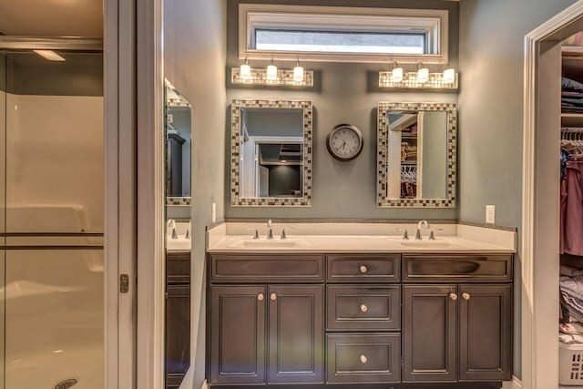 full bathroom featuring double vanity, a spacious closet, a sink, and a shower stall