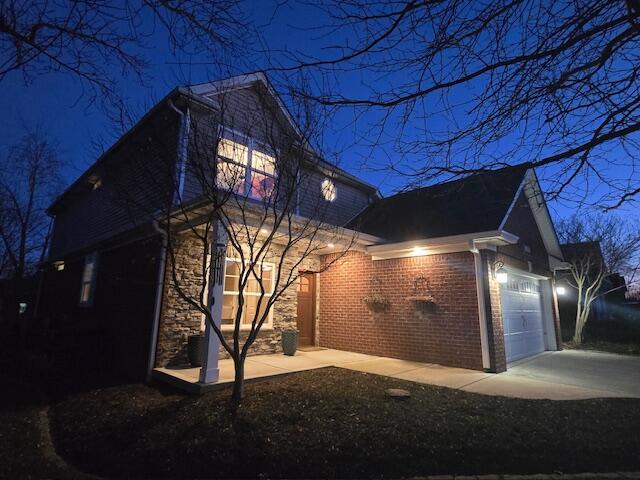 view of side of property with stone siding, brick siding, driveway, and an attached garage