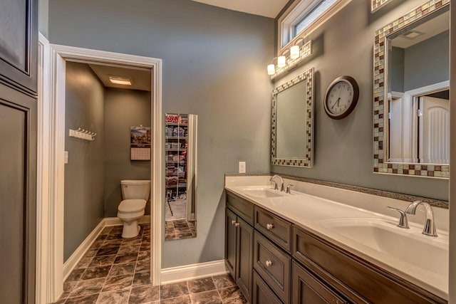 full bathroom featuring toilet, double vanity, baseboards, and a sink