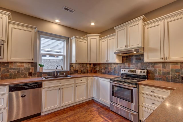 kitchen featuring dark wood-style flooring, decorative backsplash, appliances with stainless steel finishes, a sink, and under cabinet range hood