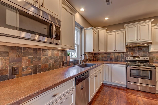 kitchen featuring dark wood-style flooring, stainless steel appliances, tasteful backsplash, a sink, and under cabinet range hood