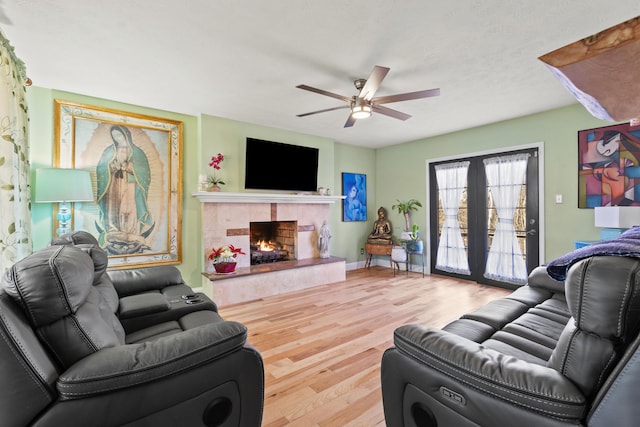 living area with a textured ceiling, a tile fireplace, wood finished floors, a ceiling fan, and baseboards