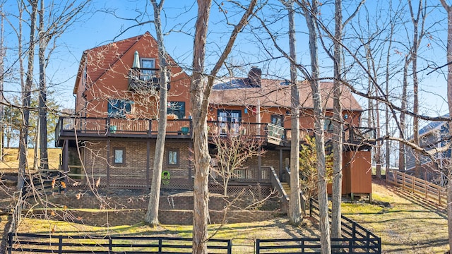 rear view of house with brick siding, a chimney, fence, and a balcony