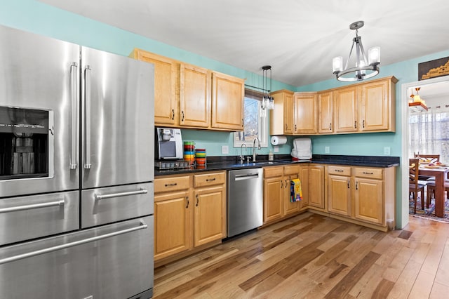 kitchen with light wood-style flooring, stainless steel appliances, a sink, dark countertops, and decorative light fixtures