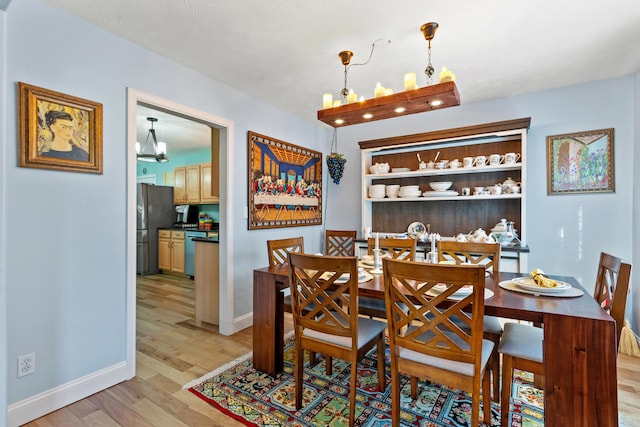 dining area featuring light wood-type flooring, baseboards, and an inviting chandelier