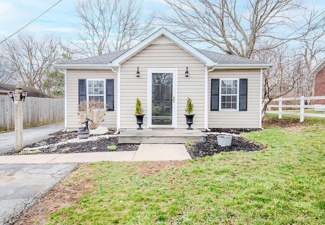 bungalow-style home with a front yard, roof with shingles, and fence