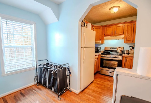 kitchen with light wood-style floors, freestanding refrigerator, light countertops, under cabinet range hood, and stainless steel range with gas cooktop