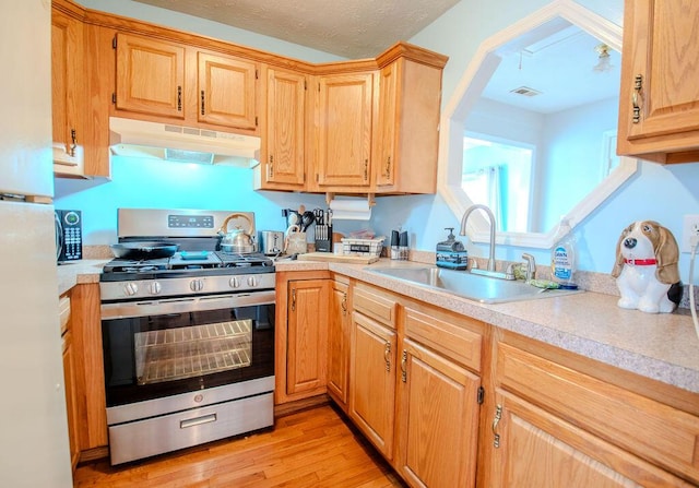 kitchen featuring light countertops, stainless steel gas range oven, a sink, and under cabinet range hood