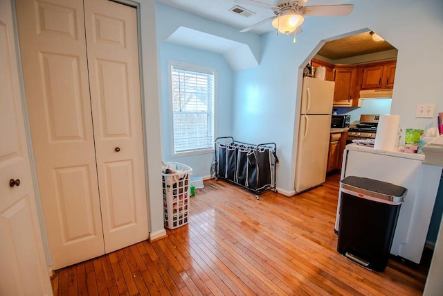 kitchen with visible vents, brown cabinetry, gas range, freestanding refrigerator, and light wood-type flooring