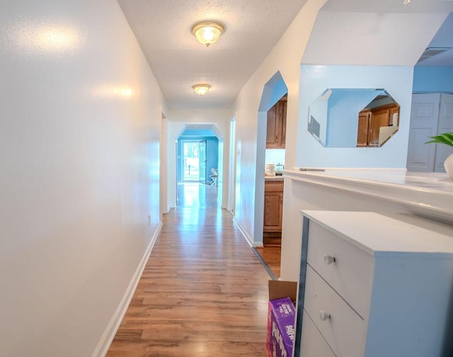 hall with arched walkways, a textured ceiling, light wood-style flooring, and baseboards