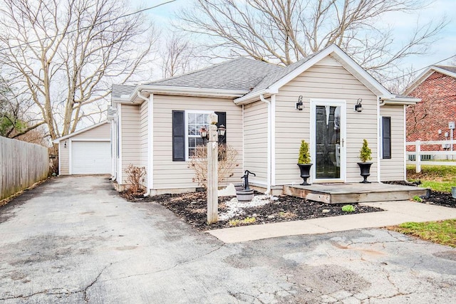 bungalow-style house featuring a shingled roof, an outbuilding, fence, and a garage