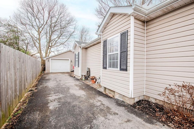 view of side of property with an outbuilding, driveway, a detached garage, and fence