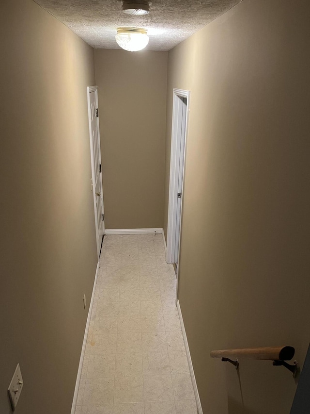 hall with baseboards, a textured ceiling, and light floors