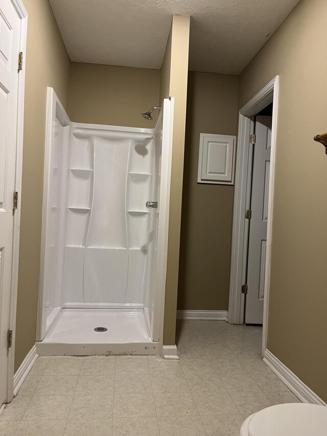 full bathroom with a textured ceiling, a shower stall, toilet, and baseboards