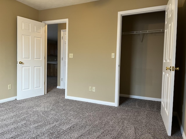 unfurnished bedroom with baseboards, dark colored carpet, and a closet