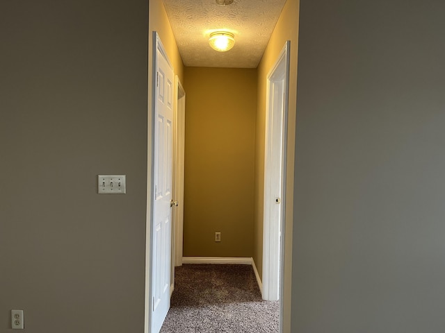 hall with a textured ceiling, carpet, and baseboards