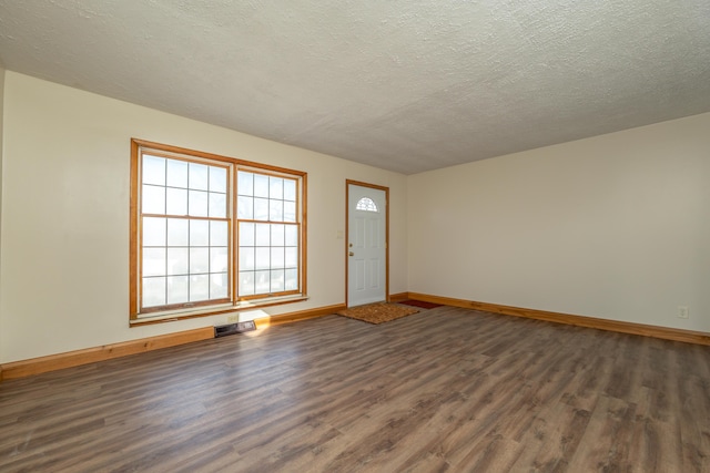 unfurnished room featuring dark wood-style floors, a textured ceiling, visible vents, and baseboards