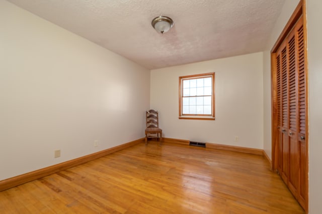 unfurnished bedroom with a textured ceiling, visible vents, baseboards, a closet, and light wood-type flooring