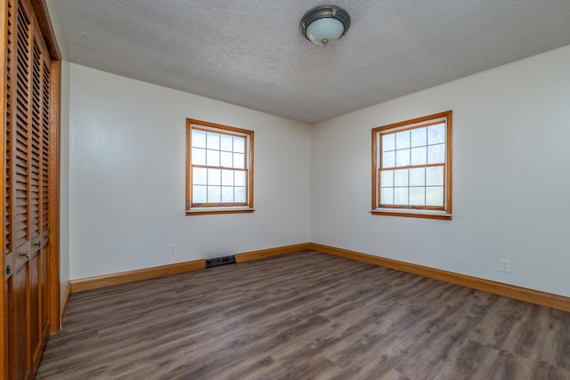 unfurnished room featuring a textured ceiling, dark wood finished floors, visible vents, and baseboards