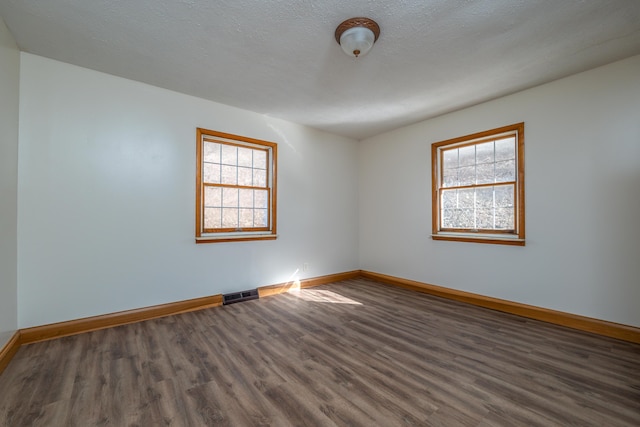 empty room with baseboards, a textured ceiling, visible vents, and wood finished floors