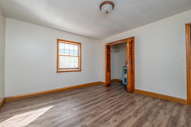 unfurnished bedroom featuring a closet, a textured ceiling, baseboards, and wood finished floors