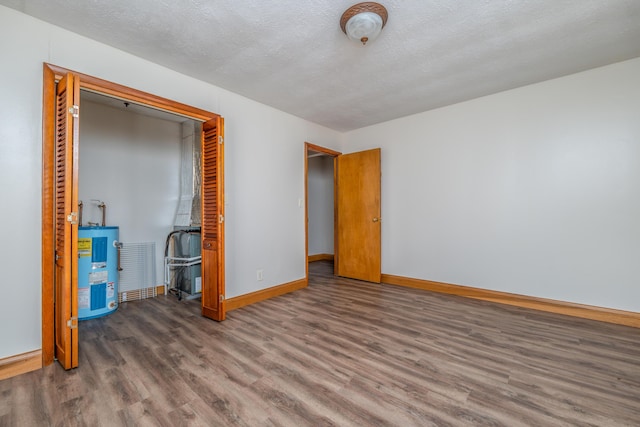 unfurnished bedroom with a textured ceiling, wood finished floors, baseboards, water heater, and a closet