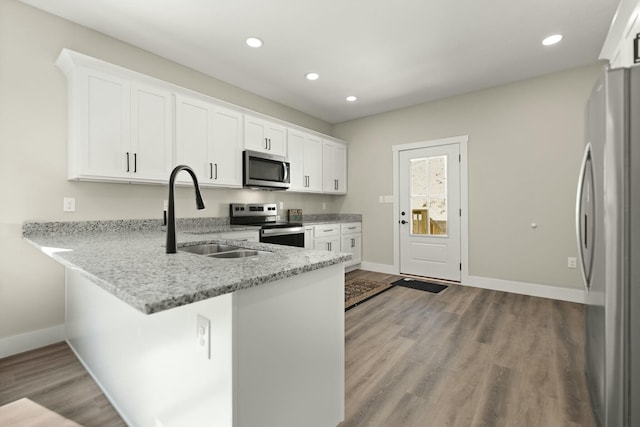 kitchen with light stone counters, a peninsula, a sink, white cabinets, and appliances with stainless steel finishes