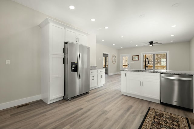 kitchen with white cabinets, light stone counters, stainless steel appliances, a sink, and recessed lighting