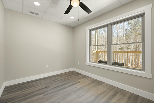 spare room featuring baseboards, visible vents, dark wood finished floors, and a drop ceiling