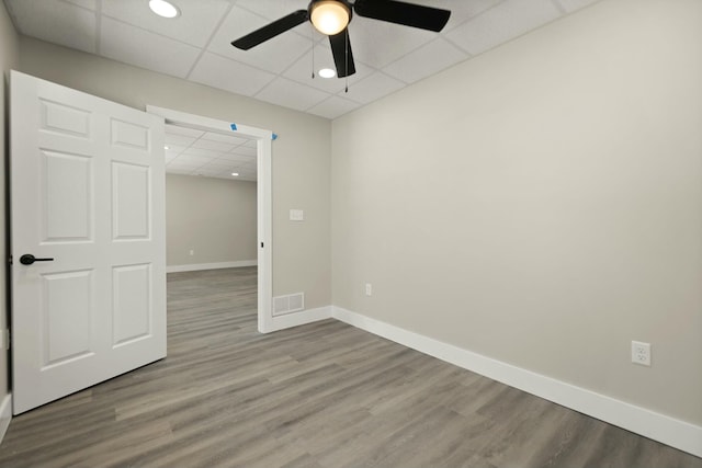 empty room with a paneled ceiling, baseboards, visible vents, and wood finished floors