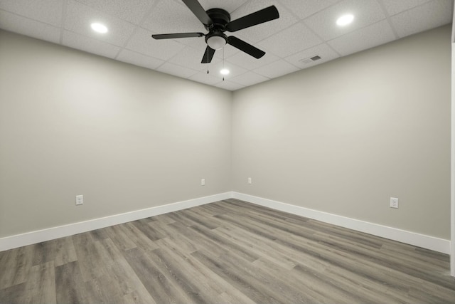 empty room with a paneled ceiling, recessed lighting, wood finished floors, visible vents, and baseboards