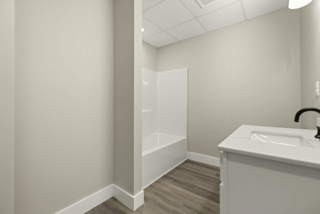 full bath with shower / bath combination, vanity, wood finished floors, a drop ceiling, and baseboards