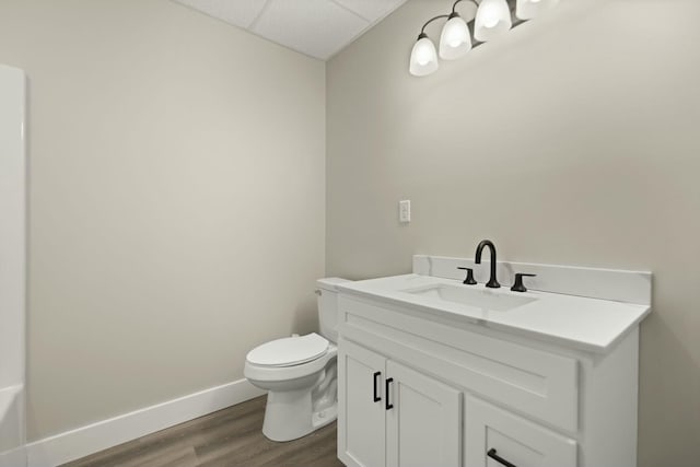 bathroom with toilet, vanity, wood finished floors, a drop ceiling, and baseboards