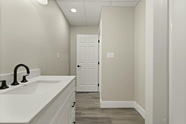 bathroom with a drop ceiling, wood finished floors, vanity, and baseboards