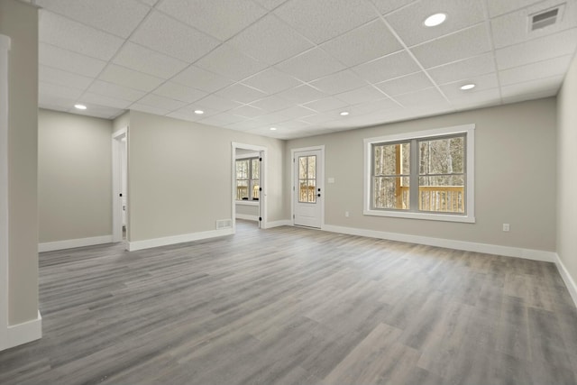 unfurnished living room featuring baseboards, a drop ceiling, and wood finished floors