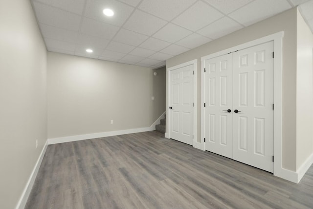 finished below grade area featuring stairway, baseboards, a drop ceiling, and wood finished floors