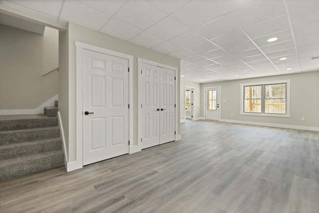 basement featuring a drop ceiling, recessed lighting, baseboards, stairs, and light wood finished floors