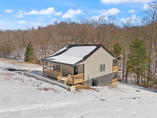 snow covered property with central AC, a porch, and a view of trees