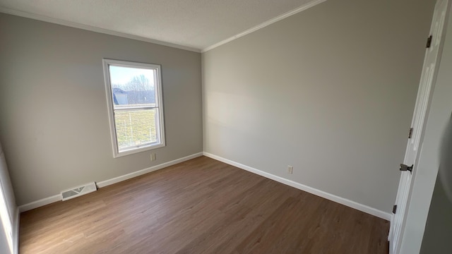 unfurnished room featuring baseboards, visible vents, crown molding, and wood finished floors