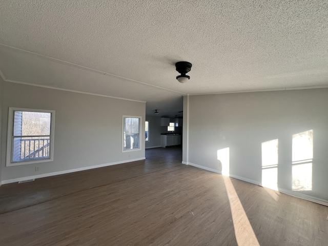 unfurnished living room featuring dark wood-style floors, plenty of natural light, a textured ceiling, and baseboards